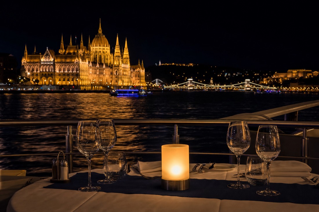 Dinner table on a Danube cruise deck with Budapest's illuminated Parliament building behind, as seen on the candlelit dinner cruise